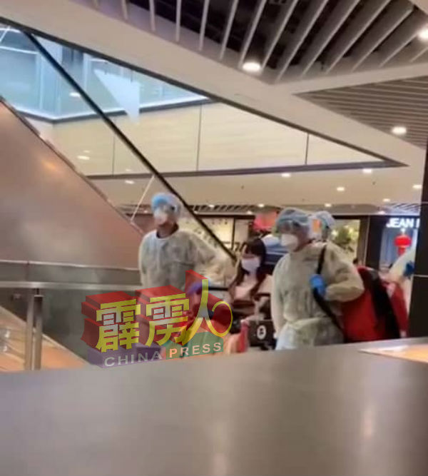 画面显示4名医护人员身穿防护服、头戴面具及口罩，全副武装般使用轮椅把一名戴着口罩的女性撤离商场的视频，是在新加坡的义顺纳福城购物商场。