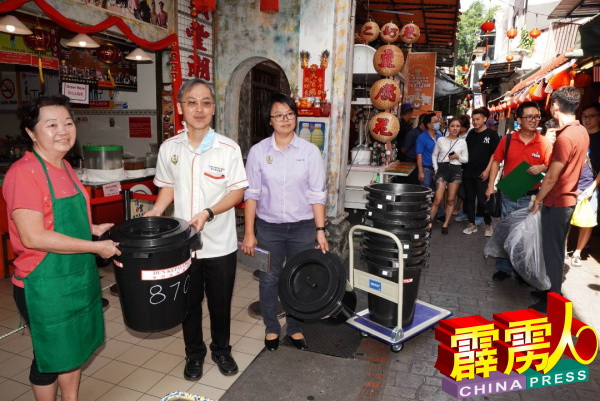 在陈慧沁（右）见证下，许崇信（左2）将垃圾桶交给商家吕银玉（左）。