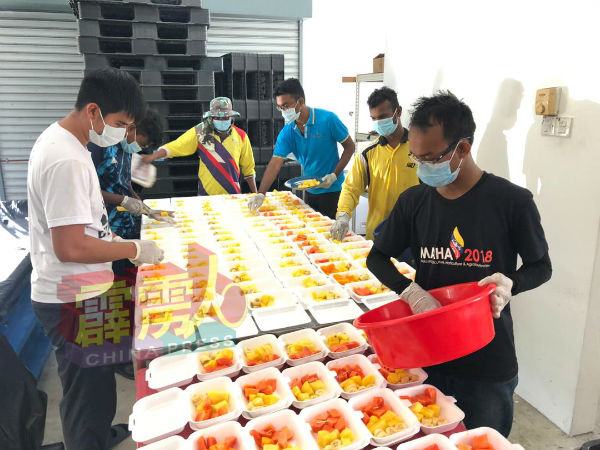 苏良添（左）与公司职员一同把水果装入盒中，方便派送给曼绒医院的前线医护人员。