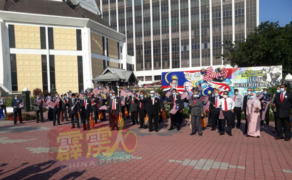 鲁迈兹（前右4）与全体职员站在市政厅前的国庆广告板，挥动手上的“辉煌条纹”，以此提醒市民谨记挂国旗。