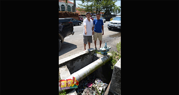 杨春松（左）指亚亦令君沟渠里堆满了空塑料罐，担心成为蚊虫繁殖地。