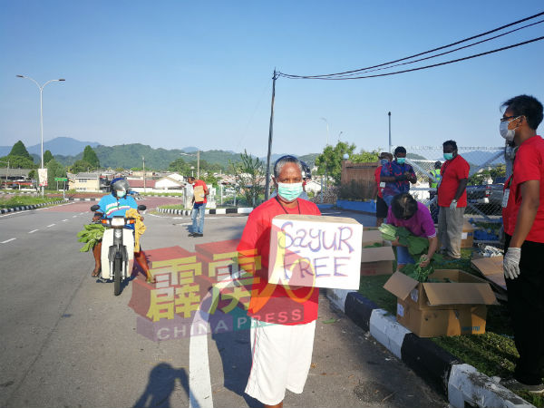 路旁手持写有“蔬菜免费”大字的纸皮箱，告知路过的行人他们正在发派免费蔬菜。