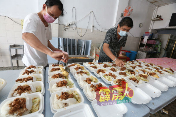 郑民伟（右）与员工把烹煮好的饭菜包装成盒。
