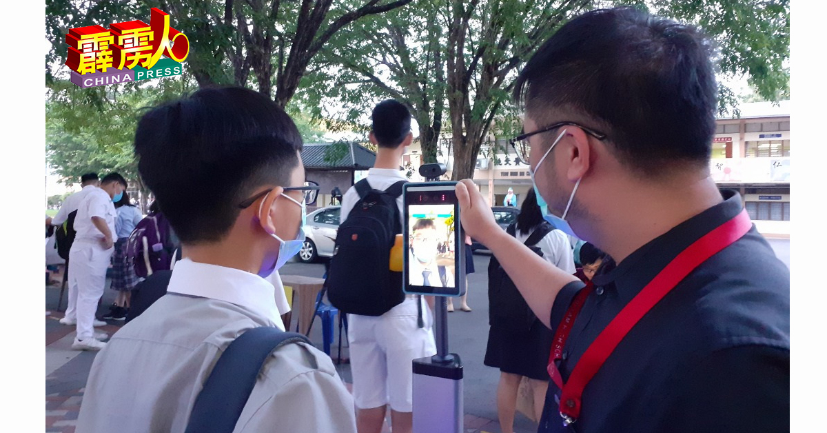 廖伟宏老师（右）使用脸部识别测温仪器为学生测量体温。