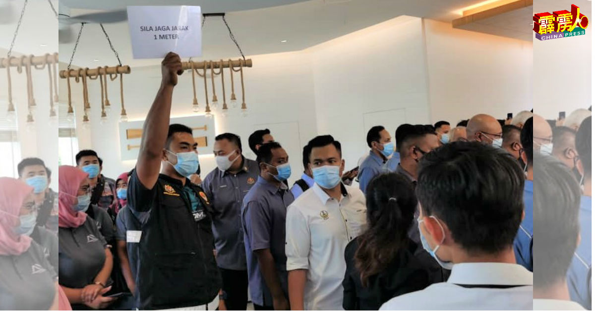 卫生局人员在展览活动上中高举“维持1公尺人身距离”告示牌，提醒出席者要遵守防疫标准程序。