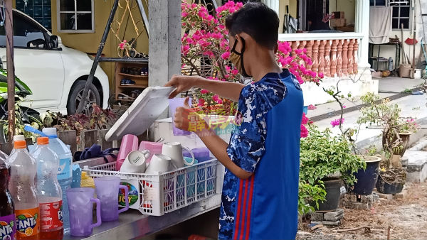 旺阿里夫在摊位当帮手，正准备饮料给顾客。