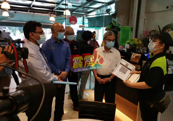 Greentown点心Cafe东主曾祝娣（右）向鲁迈兹（右2）展示该店的MySejahtera二维码及登记个资的记录簿。