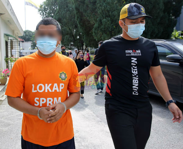因涉嫌提供假资料给霹雳州秘书的嫌犯（左）被带往法庭延扣至周日（28日），以协助调查。