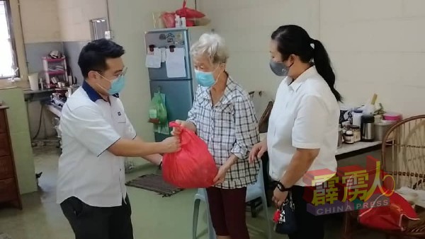 刘国南（左起）将一份物资交予一名刚完成手术后行动不便的独居老人。