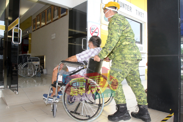 一名志愿警卫团人员协助一名坐轮椅的乐龄人士进入疫苗中心。