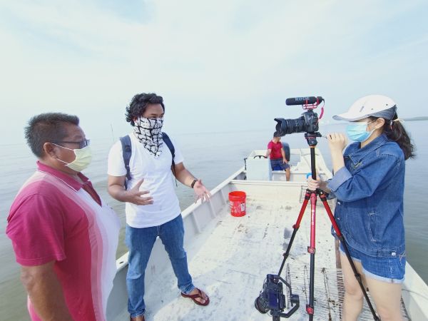 林书进（左起）在海上蚶田，现场接受蔡耀梁的视频专访；右为摄影助理曾泶炫。