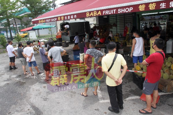民众在水果店外，排队等候购买新鲜上市的热带水果。