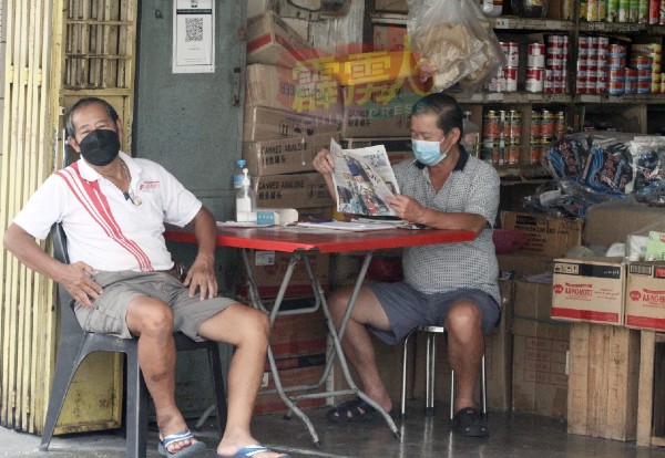 生意冷清，杂货批发商坐在店前阅读报纸，了解掌握疫情最新的资讯。