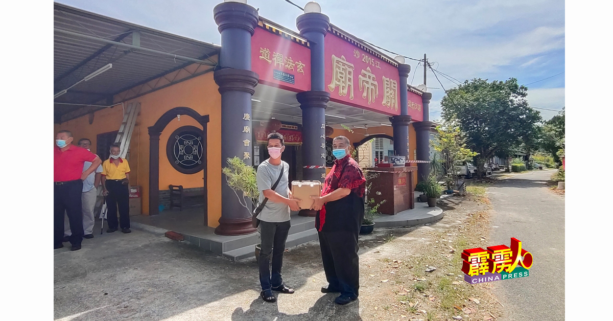 瑶伦新村村长刘振芳（左）从郭俊杰（右）手中接过饭盒与口罩。