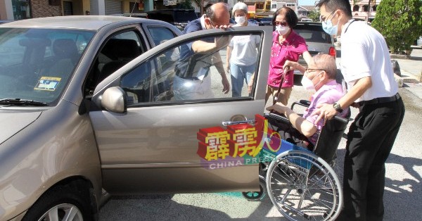 慈济义工与行动不便者的亲友，协助该名坐在轮椅的年长者上车回家。