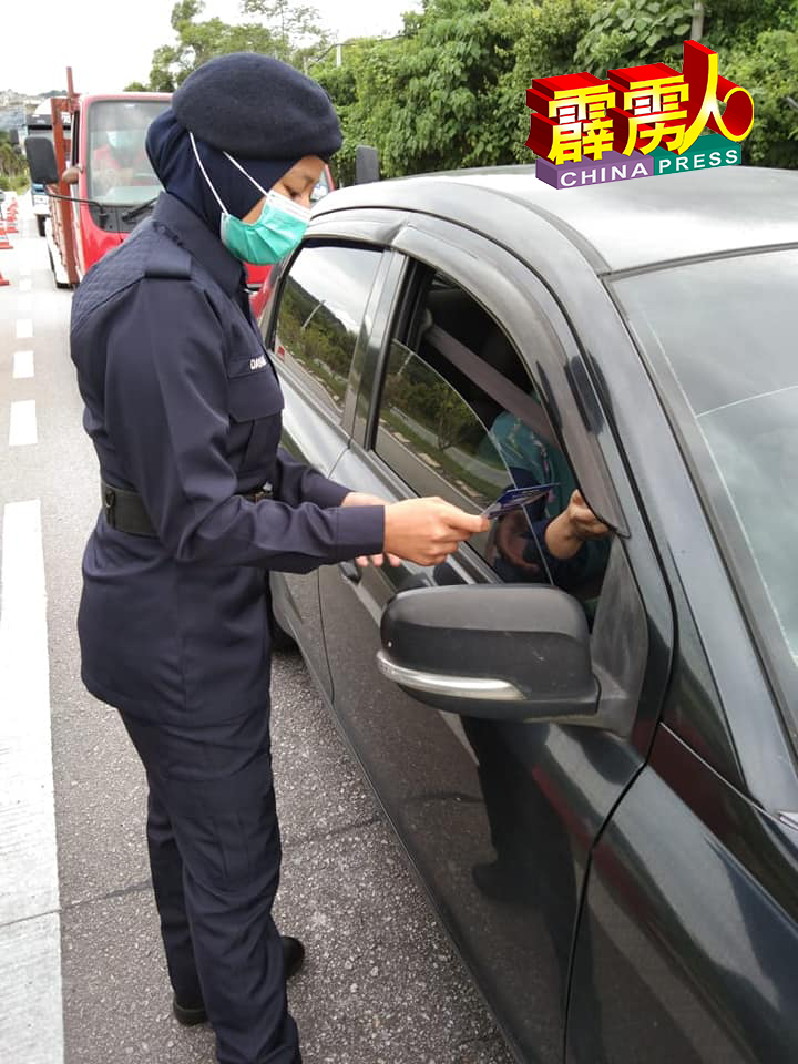 女警员派发防范诈骗手册，给经过路障的司机。