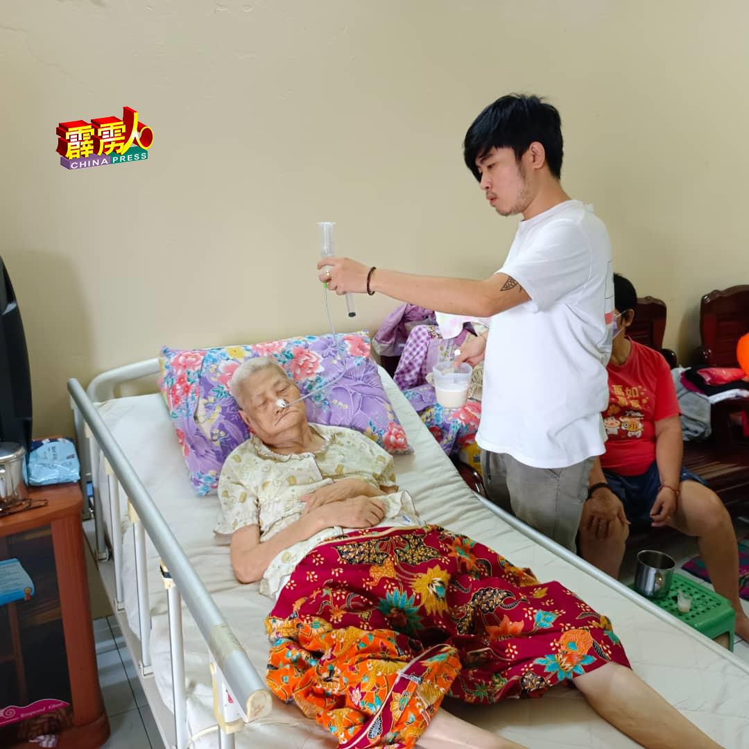 林阵伟（右）悉心照顾躺在新病床的婆婆邓秀清。