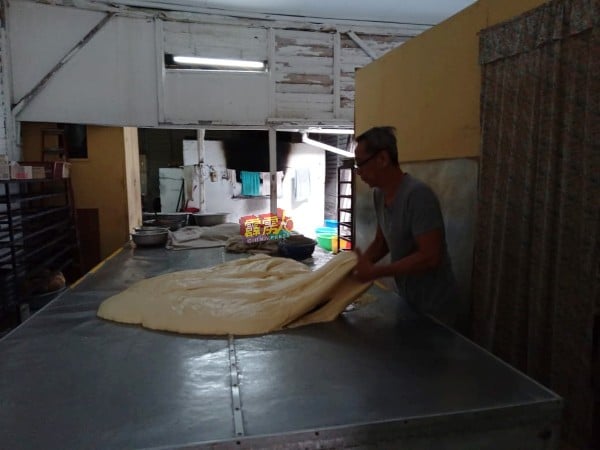 吴日利（右）在麵包厂内，准备用已逐步发酵的麵糰，开始製作各类大小麵包。