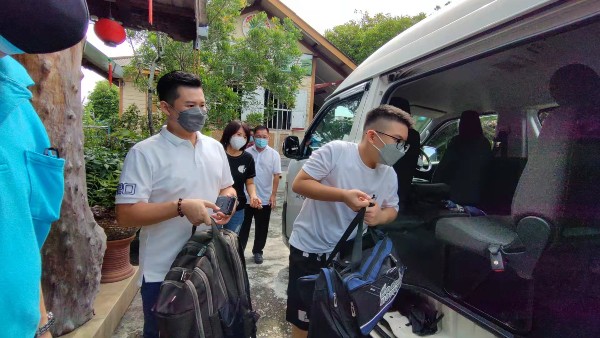 吴明峻（左起）协助儿子吴文恺把行李抬上车。