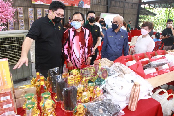 黄涵健（左起）向阿末慕尼介绍各摊位售卖的物品。