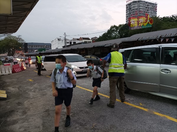 站冈的保安人员，打开车门迎接车里的小孩进入校园，同时确保交通顺畅。