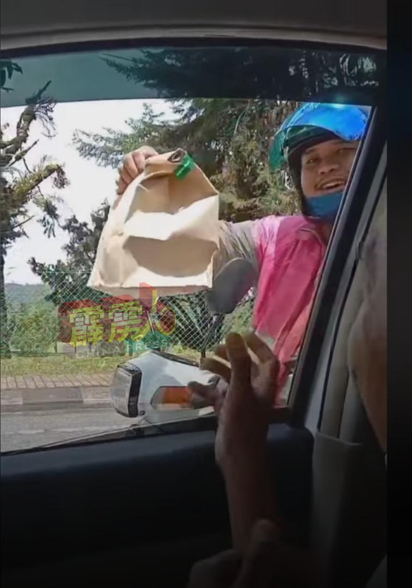 一名外卖员透过车窗，为该车内的乘客送来1份外卖。