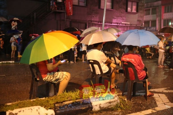 台下出席者举起雨伞或穿上雨衣，继续留在现场以表支持。