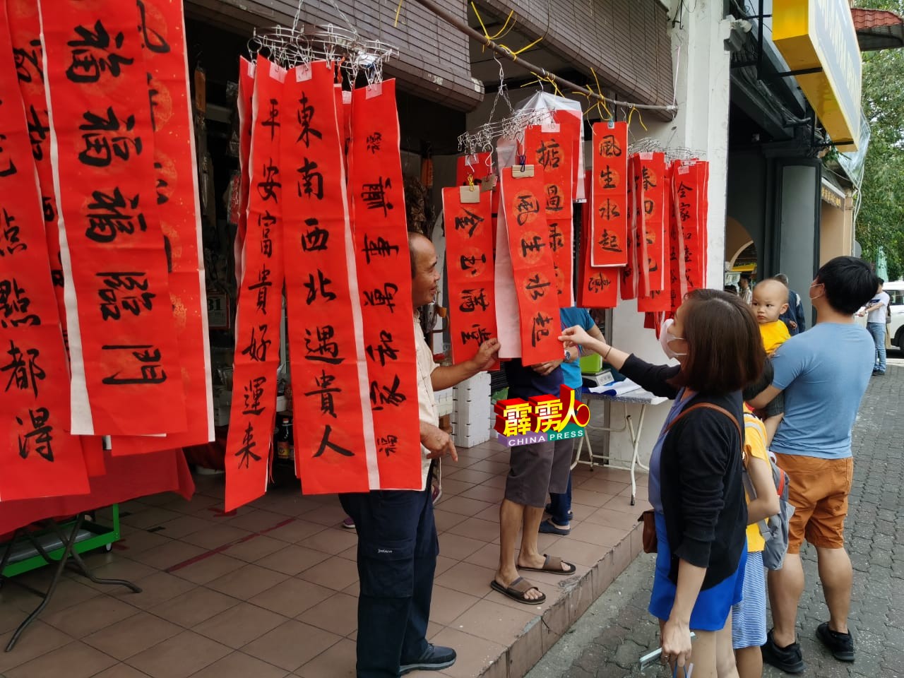 涂友成（左）在五脚基摆摊的书法摊位，吸引一些游客观赏及选购新春对联。