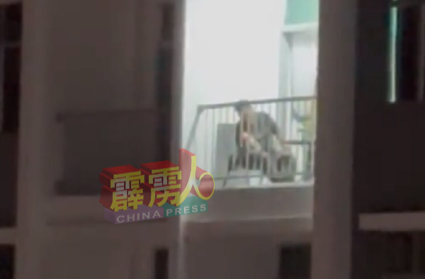 1名男子悠然地坐在公寓的阳台，在围栏朝外燃放烟花。 （视频截图）