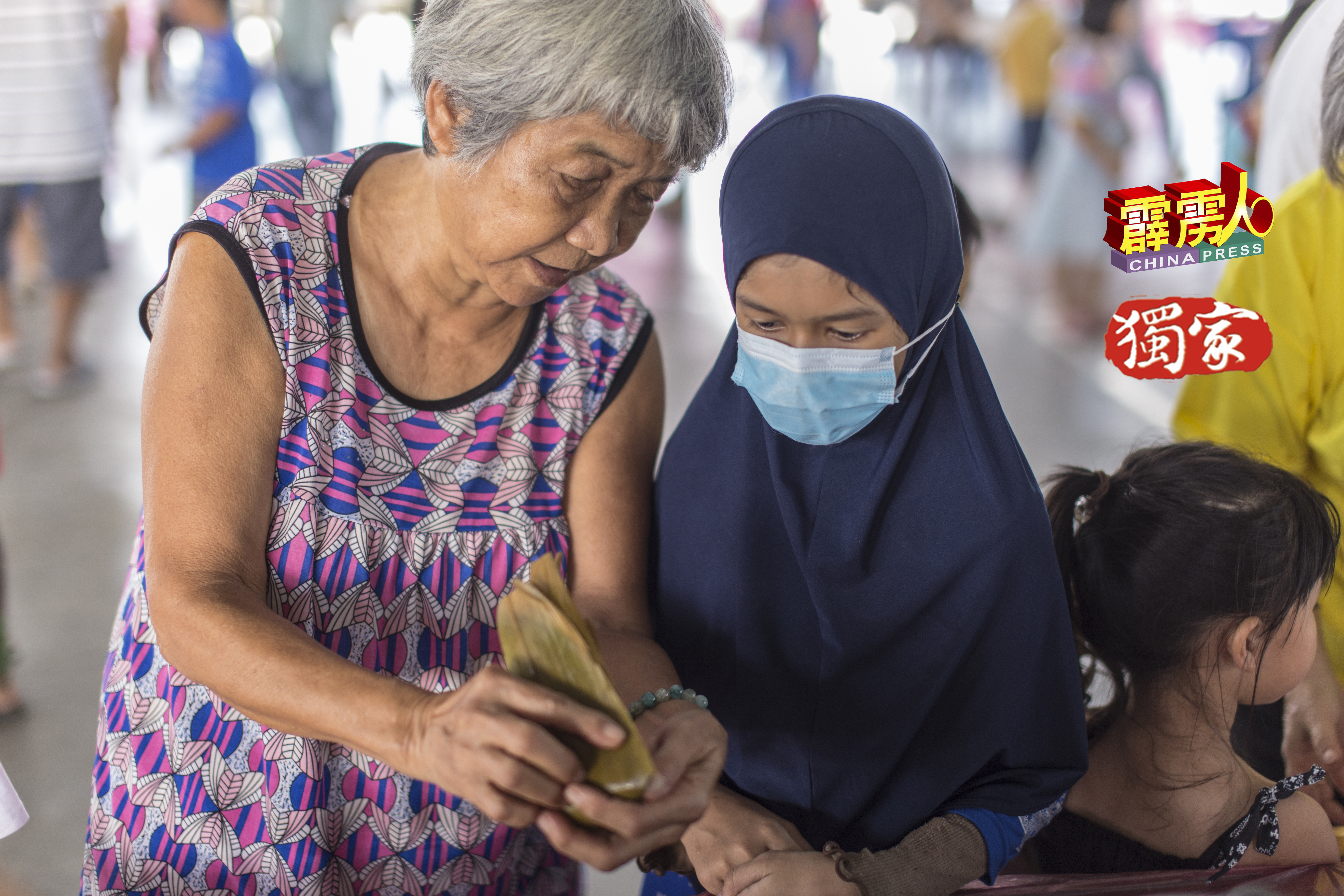 76岁老妇李阿妹，细心教导11岁马来小妹英丹裹硷水粽的手法。