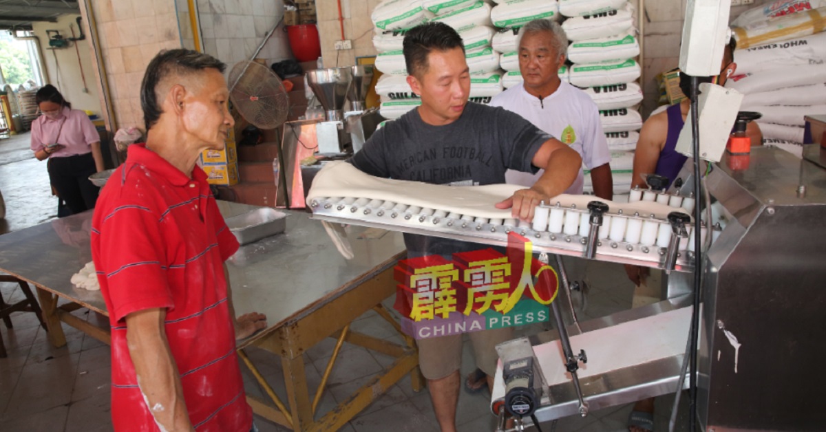 薛信伟（左2）教导伙计如何操作机器，以加快龟包的生成速度。