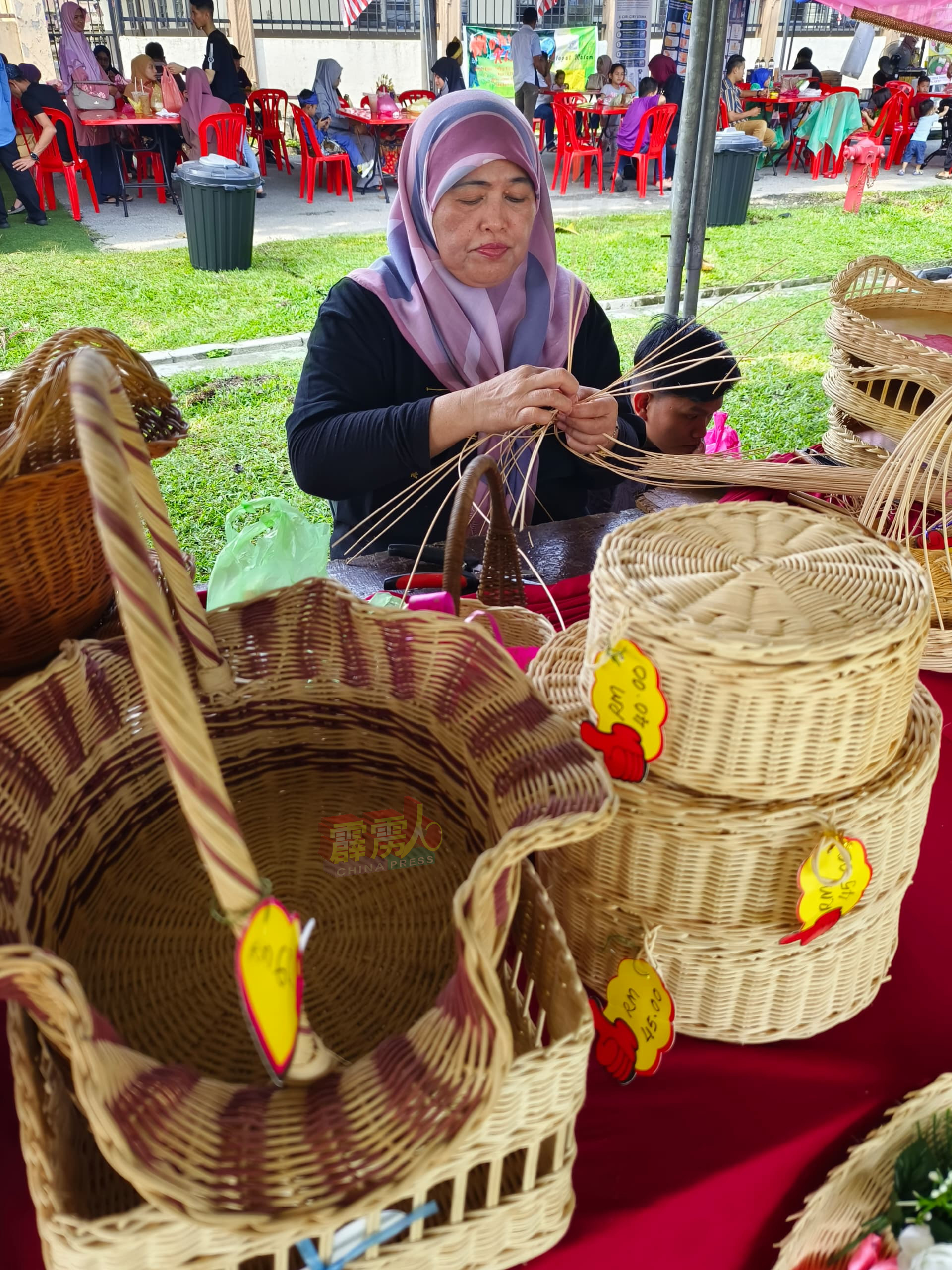 这名巫裔妇专心编织传统篮子及盒箱，并为兴趣者提供现场教学。