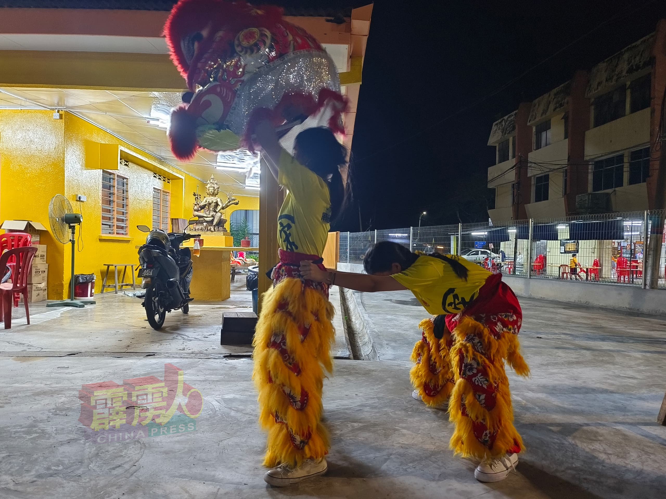 由两名女中学生共组的狮队，在夜晚抬着狮头，积极训练。