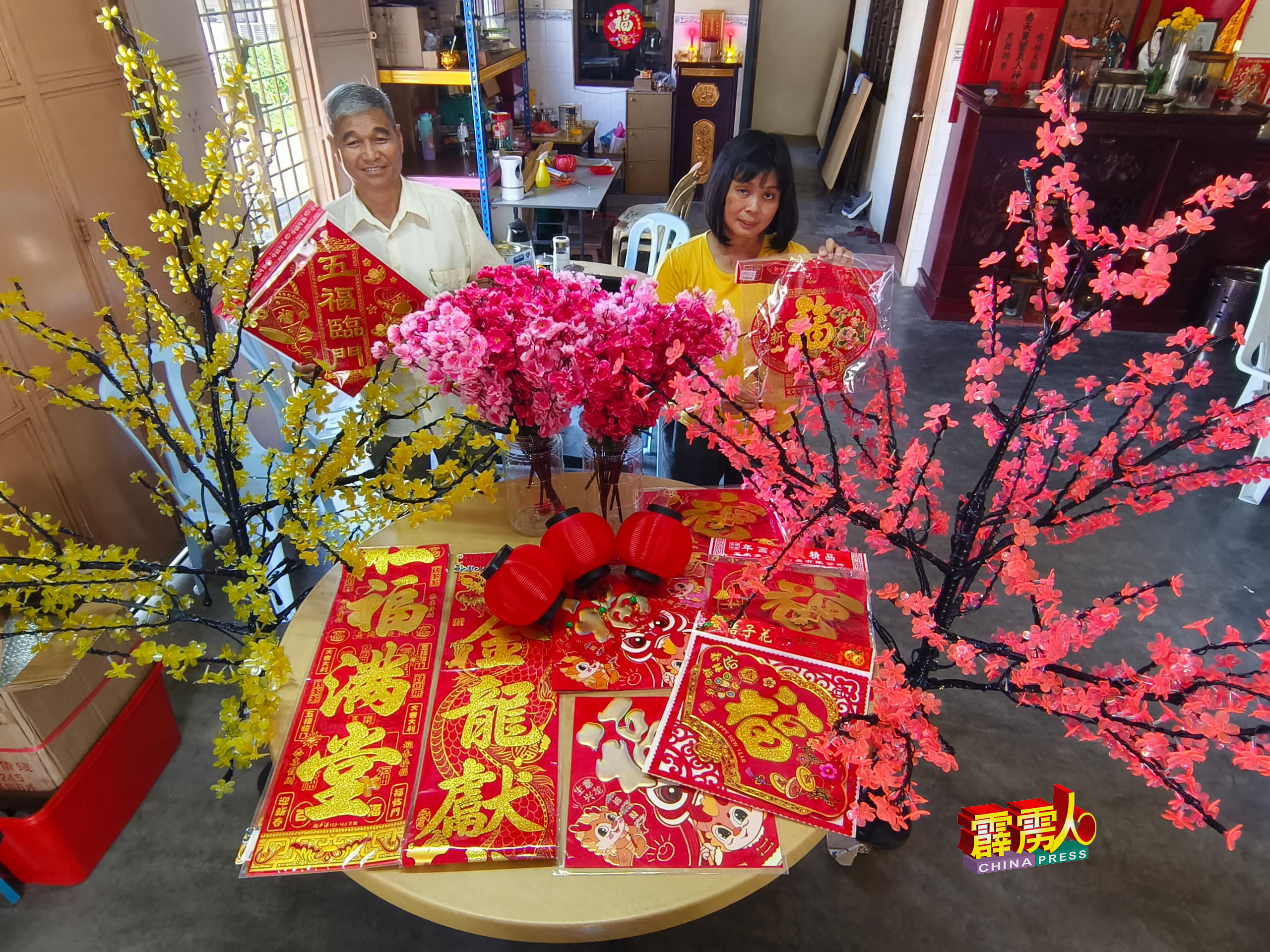 梁德文（左）与潘美云（右），展示新春打卡点的装饰品及LED桃花树。