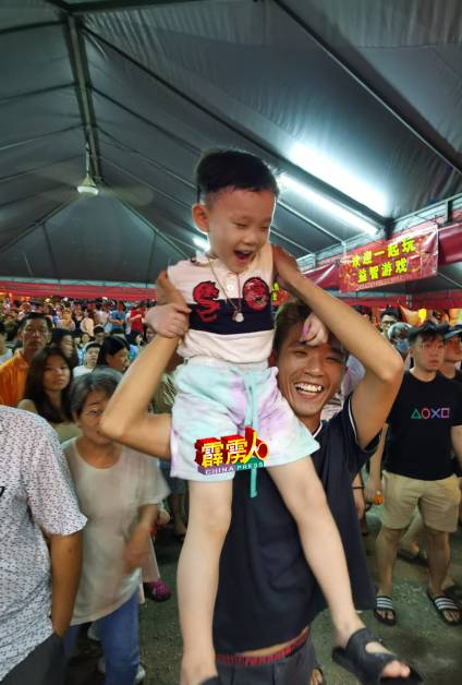 杨伟亨让孩子坐在肩上，一起看抛柑活动。