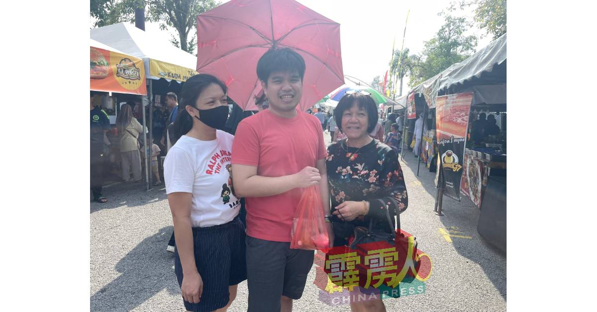 尽管太阳猛烈，张桂莲（右）与孩子一同撑伞逛市集，丝毫不减兴致。
