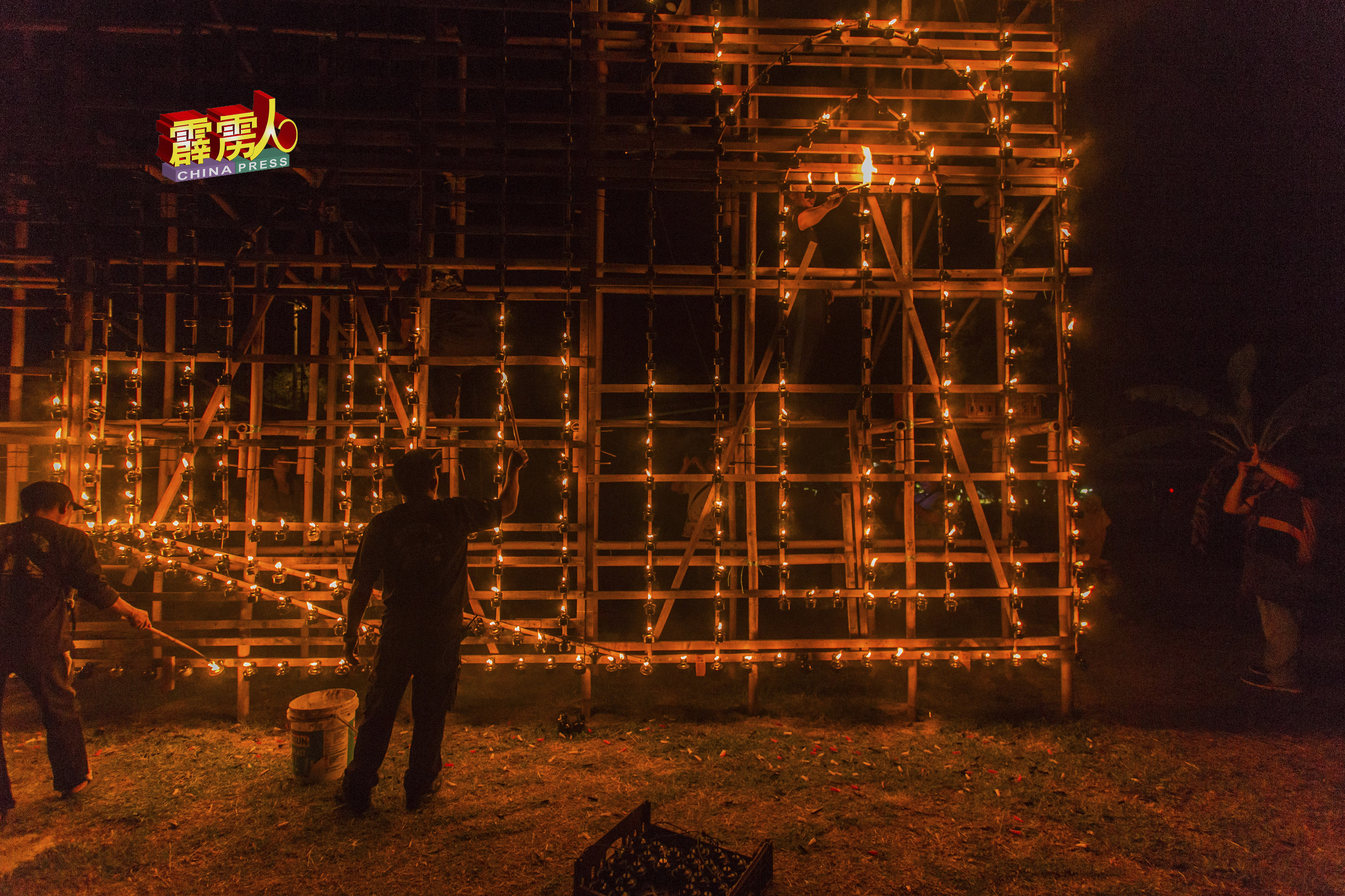 一名工作人员指挥竹棚架上的工作人员，点燃遗漏的土油灯。