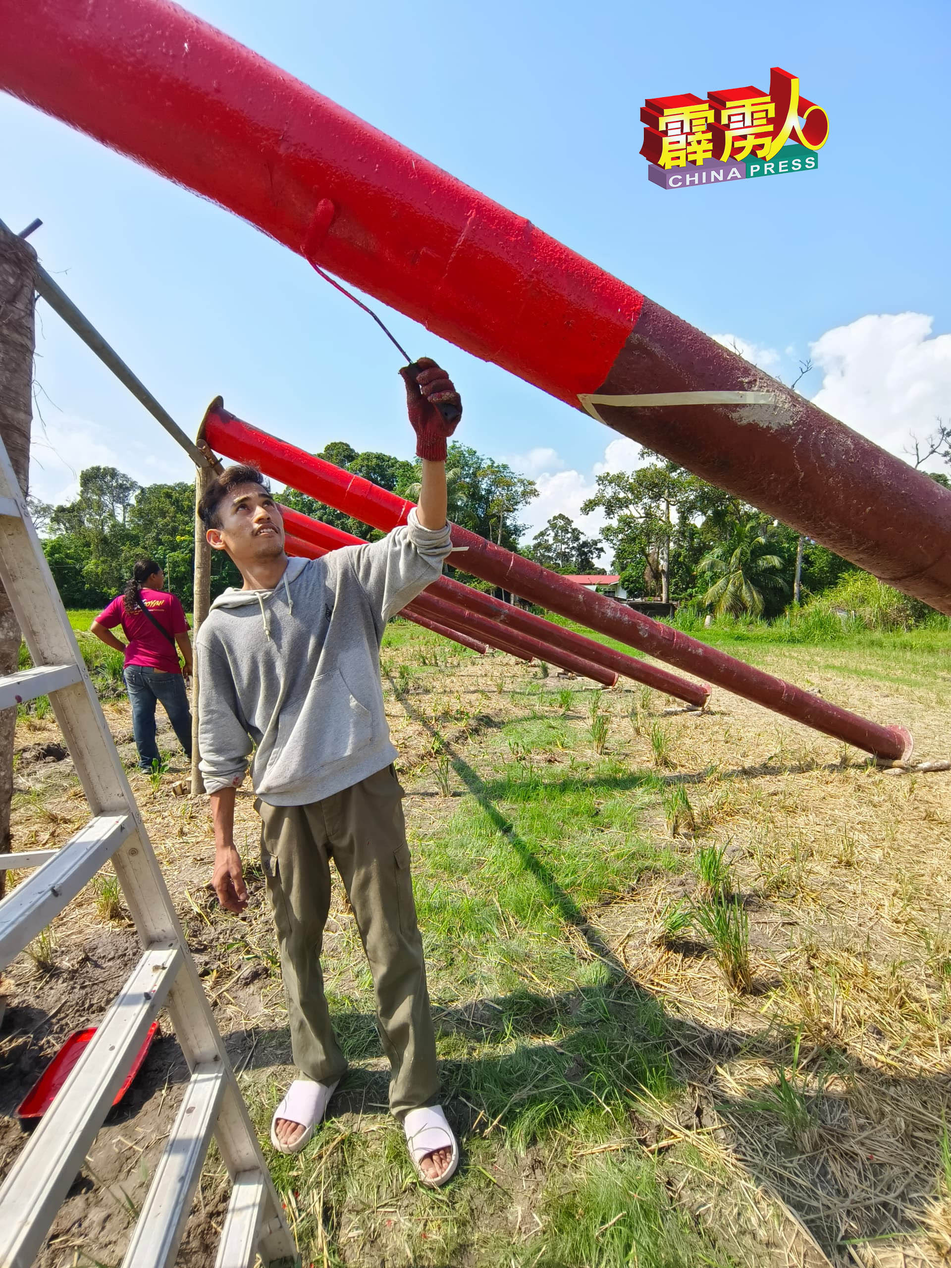 这名外号叫“光头佬“的马来村民，在烈阳下为大炮涂上红漆。