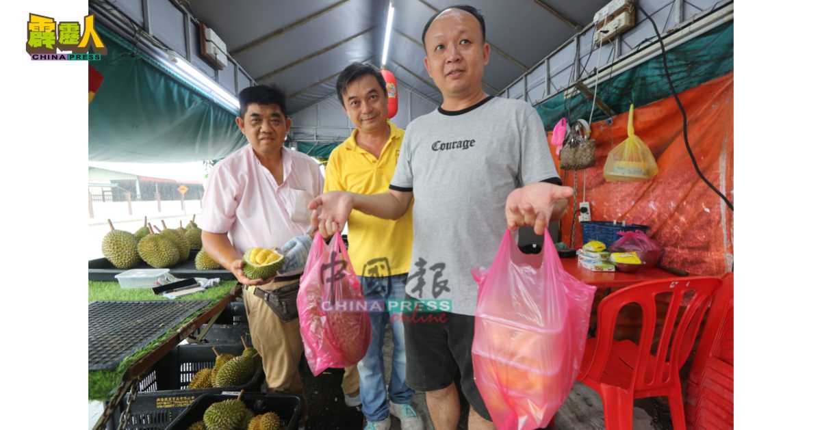 购买榴槤还获额外赠送,严植兴(右)感到惊喜。左为昆仑喇叭双王榴槤摊位东主林德荣与伙计。