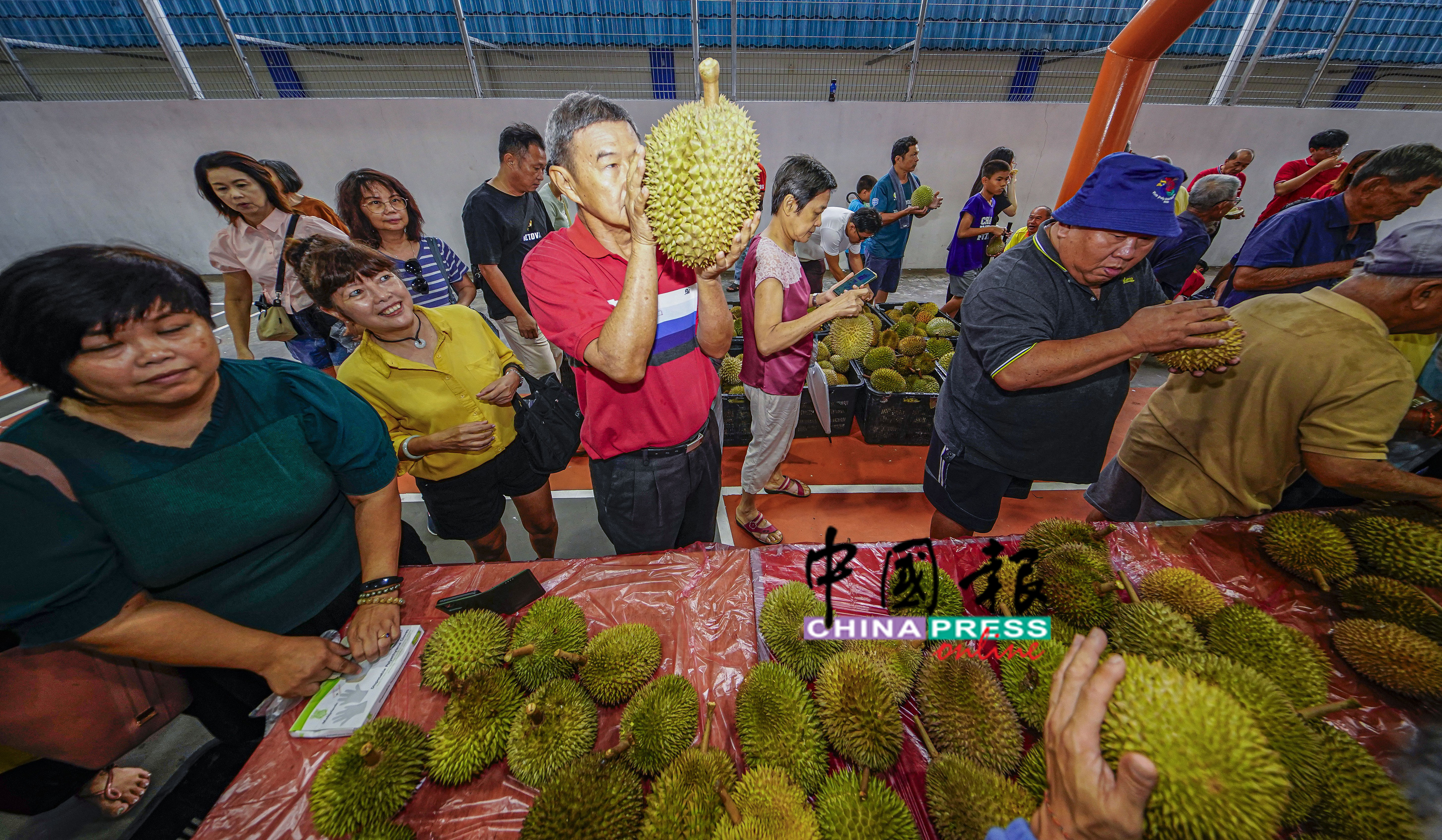 一名男子拿起一个巨大的榴槤来闻，羡煞旁人。
