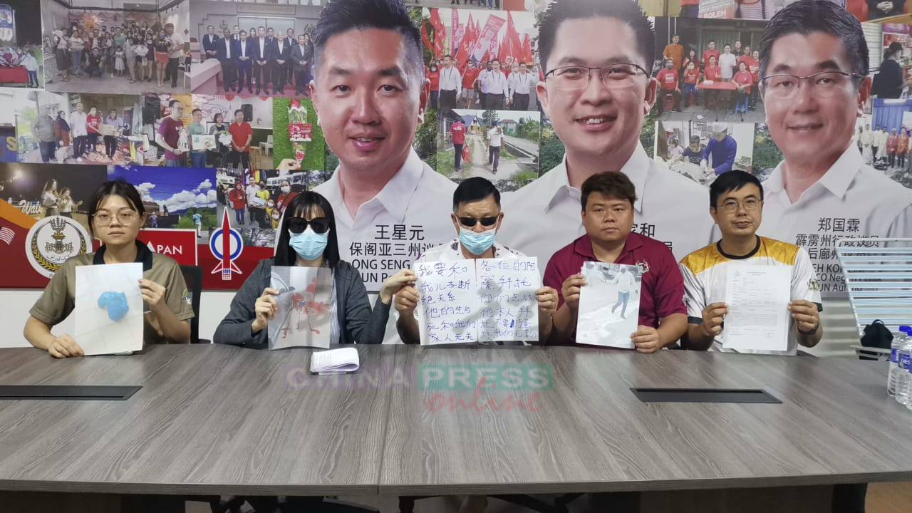 马清枝(中)展示2张自己写的直幅,宣称与儿子脱离关系,左2为其女儿,右起为保阁亚三村长叶天财与黄良伟,左为县发展官戴汇霖。