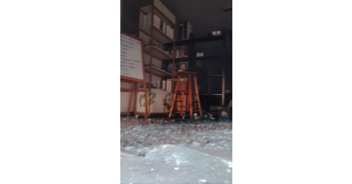 店铺铁卷门已弯曲，店内其中一道玻璃门破碎，地面布满玻璃碎片，一片狼藉。（视频截图）