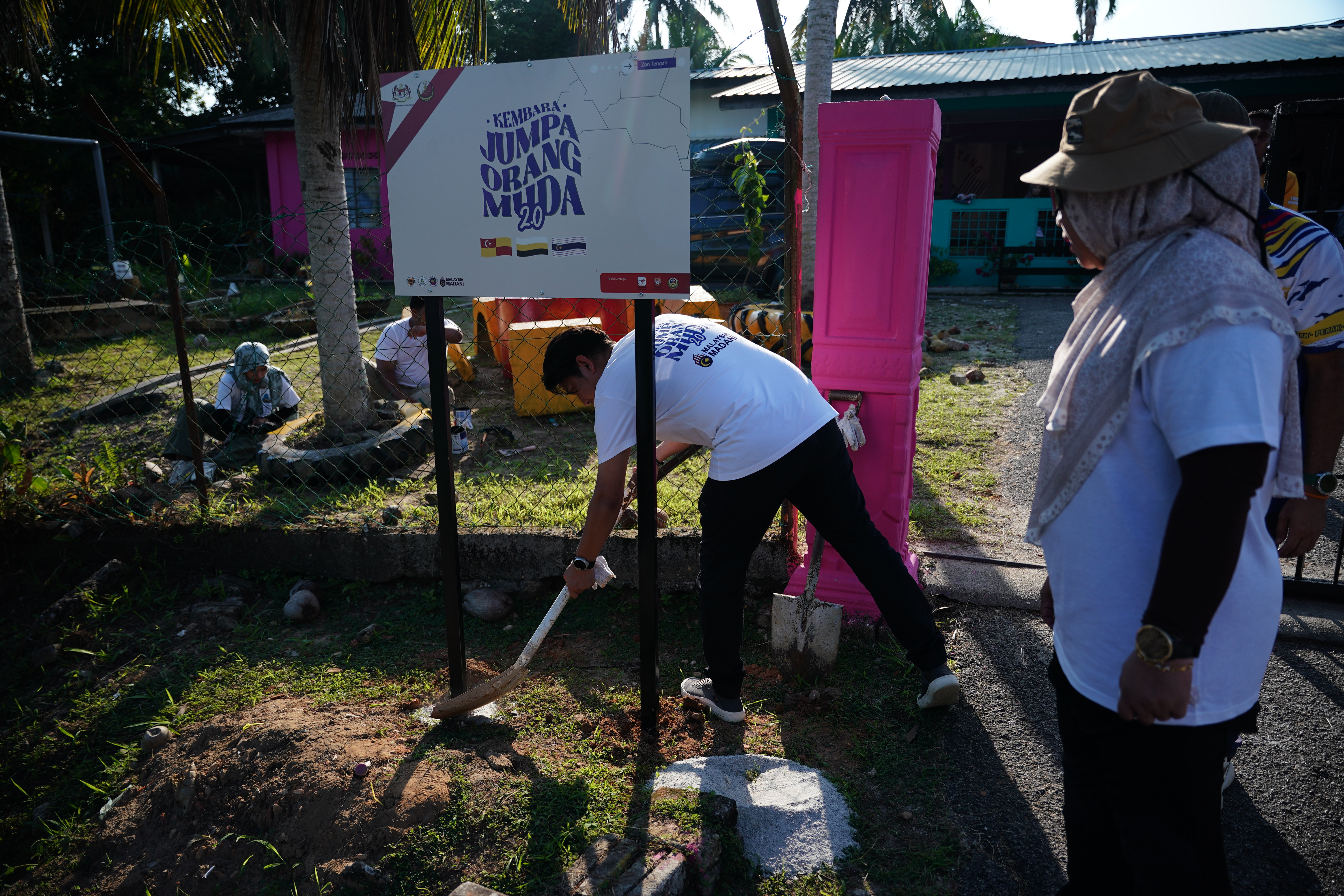 阿当阿里(右)持著铲子为“会见青年行程“牌子堆土。</p><figcaption class=